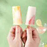 Set x2 moldes para paletas de helado con trozos de fruta, sostenidos por manos, con copa de cóctel de fondo.