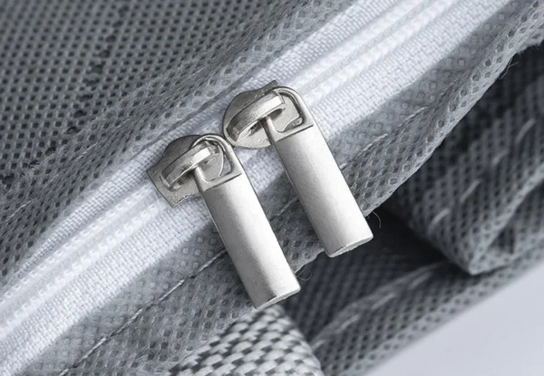 Bolsa plegable para closet con dos tiradores de cremallera plateados sobre tela gris texturizada.