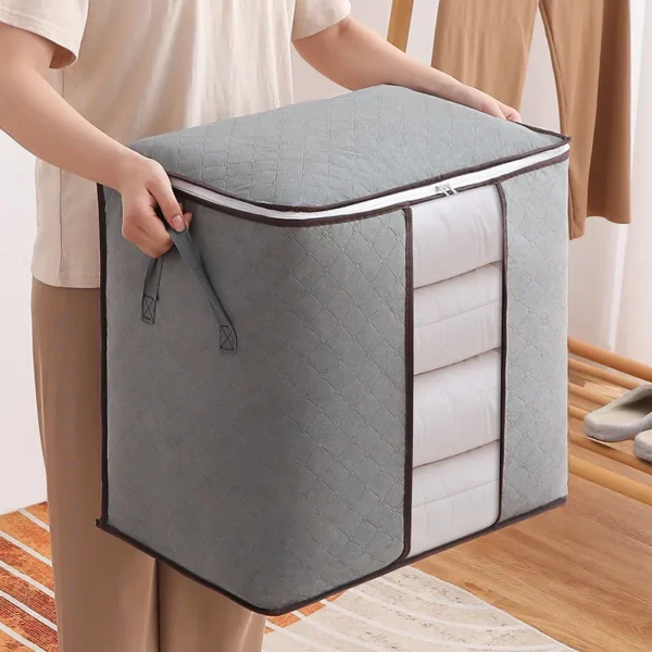 Bolsa plegable gris con cremallera para closet, con compartimento transparente que muestra edredones apilados.