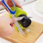 Afilador de cuchillos portátil eléctrico afila tijeras en tabla de madera.