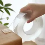 Cinta doble faz de silicona transparente lavable de 3 metros, fijando un trozo a un mueble de madera.