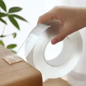 Cinta doble faz de silicona transparente lavable de 3 metros, fijando un trozo a un mueble de madera.