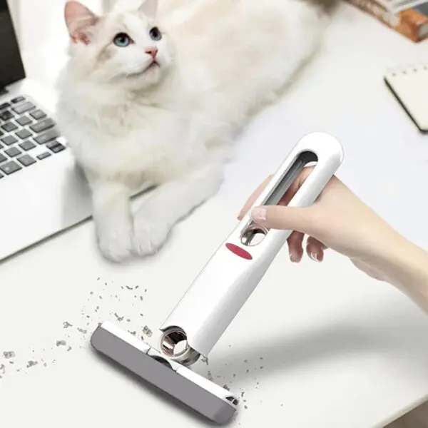 Mini trapeador para escritorio limpiando migas cerca de un gato blanco y azul en una mesa.
