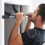 Hombre haciendo dominadas en barra de puerta, entrenamiento de fuerza en casa.