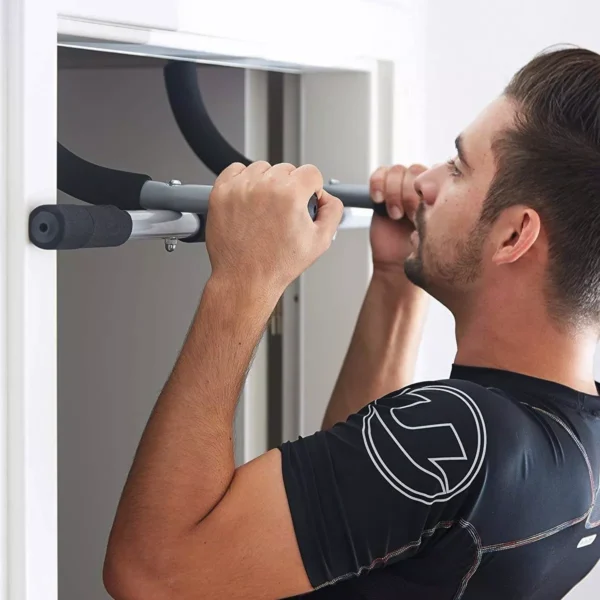 Hombre haciendo dominadas en barra de puerta, entrenamiento de fuerza en casa.