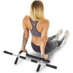 Mujer haciendo abdominales en barra para marco de puerta con piernas extendidas.