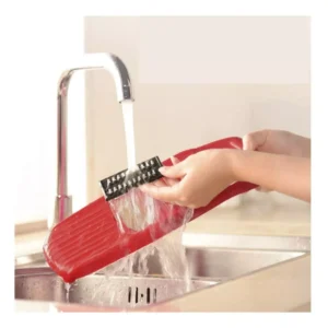 Picador y rallador multifuncional 6 en 1 rojo siendo lavado bajo un grifo abierto en el lavaplatos.