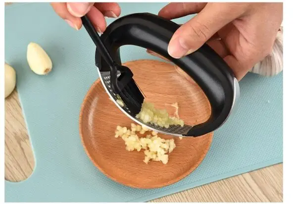 Picador ergonómico de acero inoxidable para ajo machacado en plato de madera.
