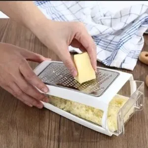 Rallador de queso con recipiente, rallando un bloque de queso amarillo en un cajón transparente.