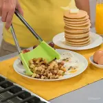 Pinzas espátula de silicona sirviendo papas, junto a huevos y tortitas.