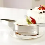 Porcionador de tortas con un trozo de pastel de frutas en un plato blanco.