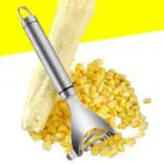 Pelador desgranador de maíz en acero inoxidable con mazorca y granos de maíz.