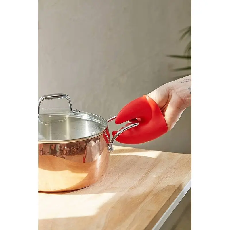 Guantes antiquemaduras de silicona rojos sujetando las asas de una olla de cobre.