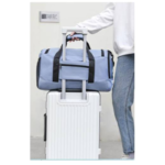 Bolso de viaje grande azul claro con compartimento frontal, apilado sobre maleta blanca con ruedas.