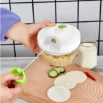 Picador de alimentos manual Picatodo con mano jalando la cuerda, sobre tabla de madera con pepino, chile y tortillas.