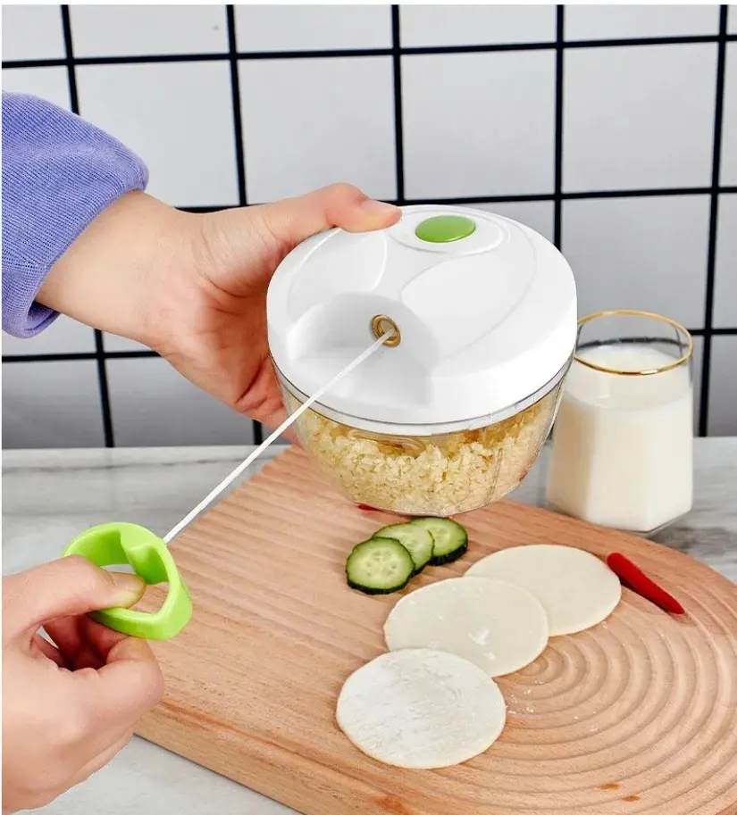Picador de alimentos manual Picatodo con mano jalando la cuerda, sobre tabla de madera con pepino, chile y tortillas.