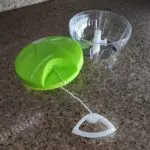 Picador de alimentos manual verde con recipiente transparente y cuerda para picar hierbas y verduras.