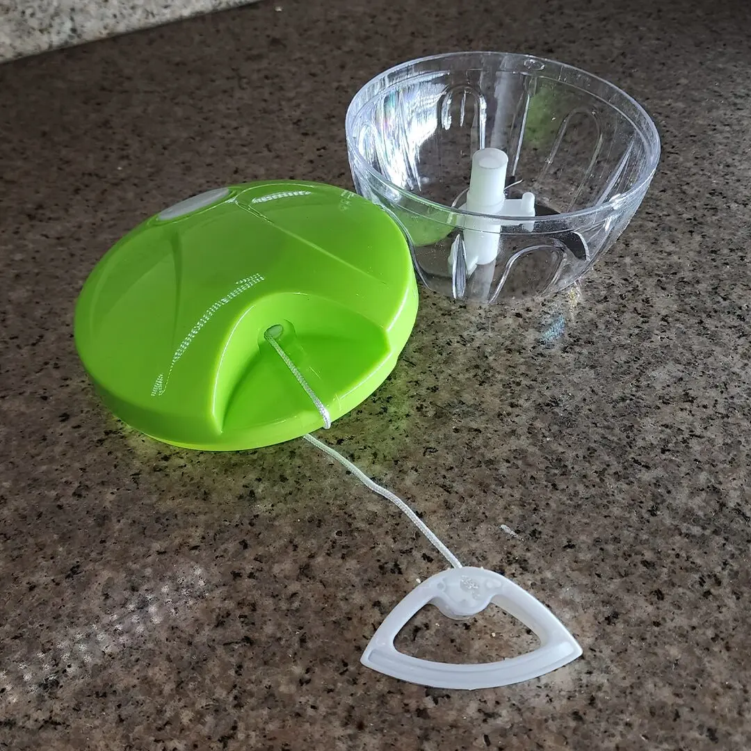 Picador de alimentos manual verde con recipiente transparente y cuerda para picar hierbas y verduras.