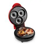 Máquina de mini donas roja con 3 donas decoradas: chocolate con maní y glaseado con frutos secos.