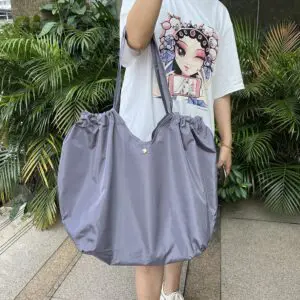 Bolso Origami gris de gran tamaño con diseño de cierre fruncido, llevado por una persona.