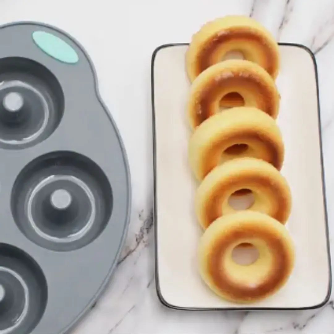 Molde de silicona para donas grises junto a cinco deliciosas donas doradas en un plato blanco.