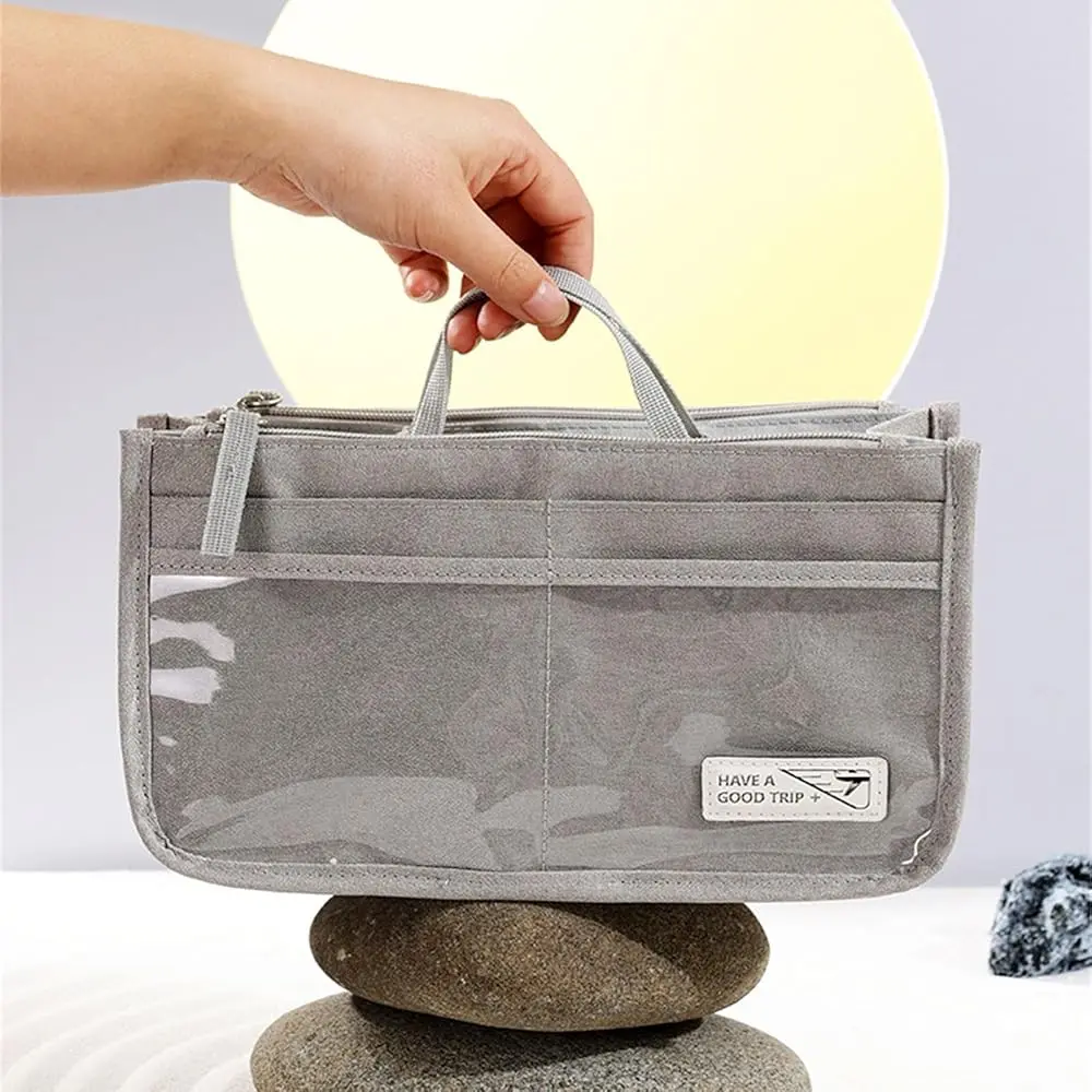 Bolso organizador gris "Oasis" con compartimentos transparentes, agarraderas y etiqueta "Have a good trip".