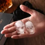Molde calavera hielera Drop con dos cubitos de hielo en forma de calavera sostenidos en una mano.