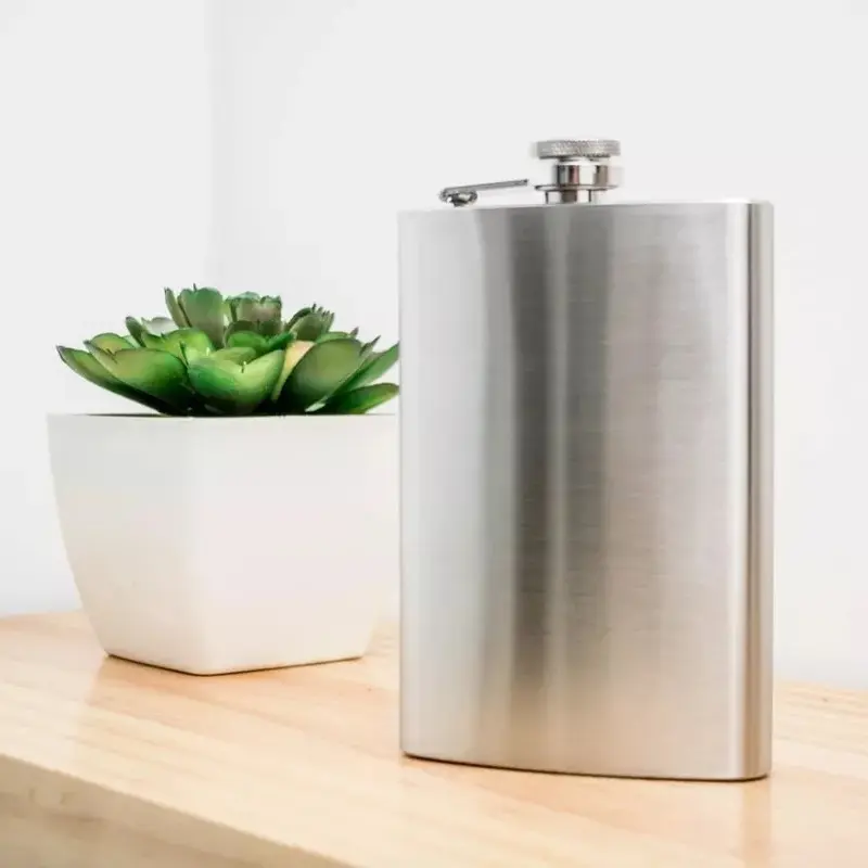 Licorera de acero inoxidable de 5 oz con tapa de rosca junto a una planta suculenta en maceta blanca.