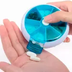 Pastillero semanal giratorio azul y blanco dispensando píldoras blancas en la palma de una mano.