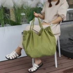 Bolso Origami verde, grande y arrugado, en mano de mujer sentada con sandalias blancas.