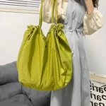 Bolso Origami verde con doble asa, diseño plegable y cierre de cordón, sostenido por una persona.
