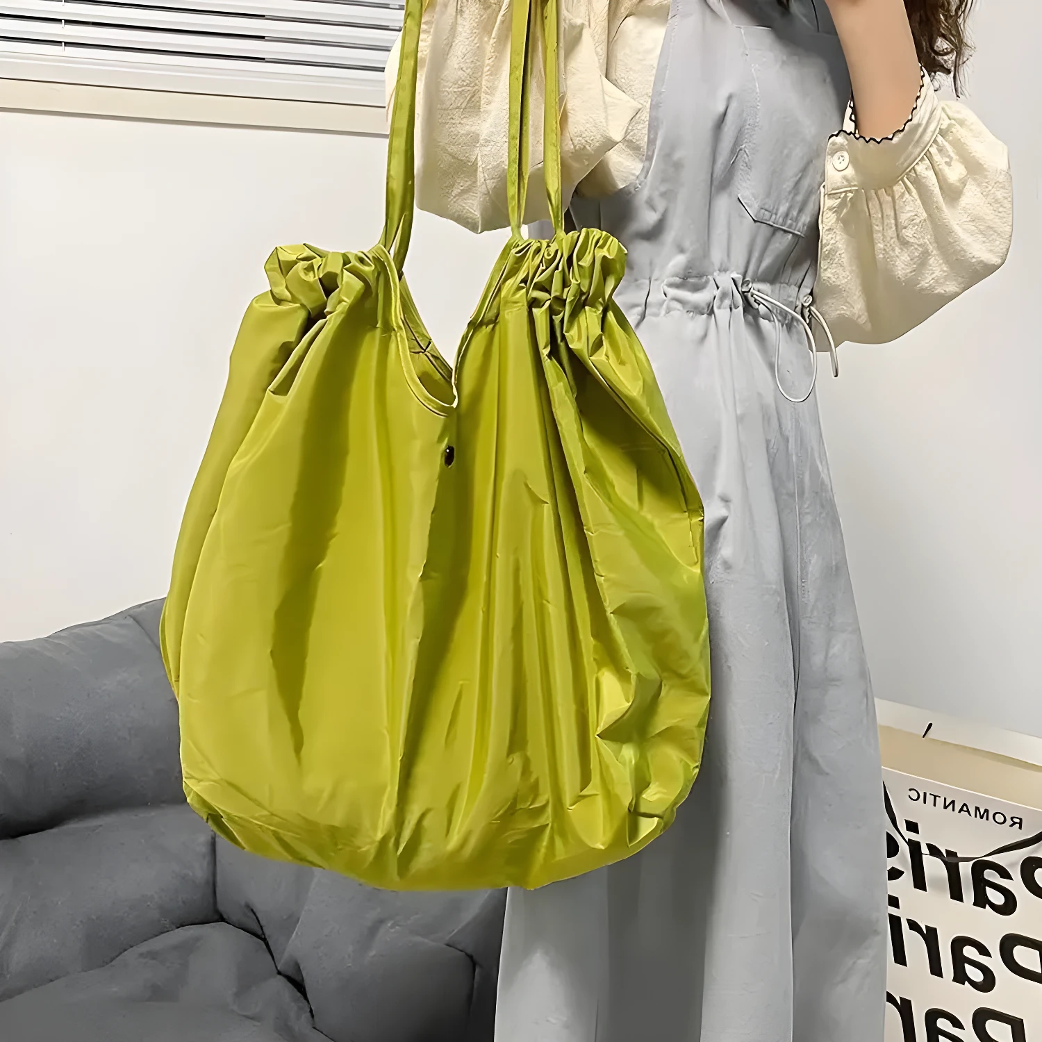 Bolso Origami verde con doble asa, diseño plegable y cierre de cordón, sostenido por una persona.