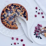 Porcionador para tortas de acero inoxidable cortando un pastel de frutos rojos y coco rallado.