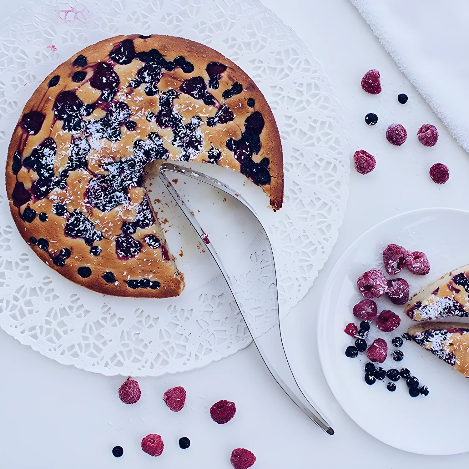 Porcionador para tortas de acero inoxidable cortando un pastel de frutos rojos y coco rallado.