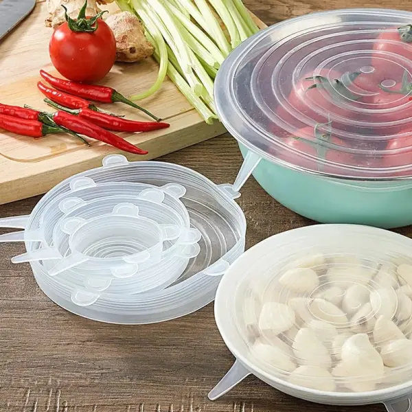 Set de 6 tapas de silicona reutilizables cubriendo varios recipientes con alimentos como tomates y ajos.