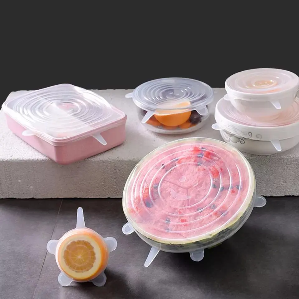 Set de 6 tapas de silicona elásticas para alimentos, cubriendo un melón, platos y frutas.