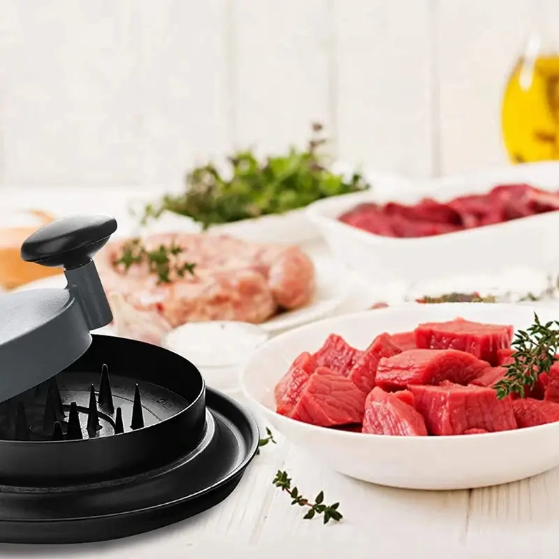 Máquina trituradora de pollo con trozos de carne cruda y hierbas frescas sobre una mesa.