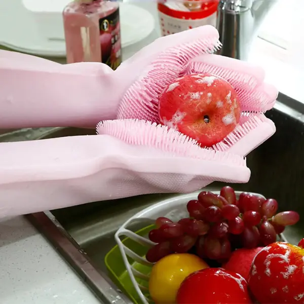 Guantes mágicos MG rosados limpiando una manzana con burbujas en un fregadero con frutas.