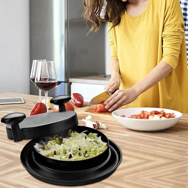 Máquina trituradora de pollo negra sobre mesa de cocina con mujer picando tomates.