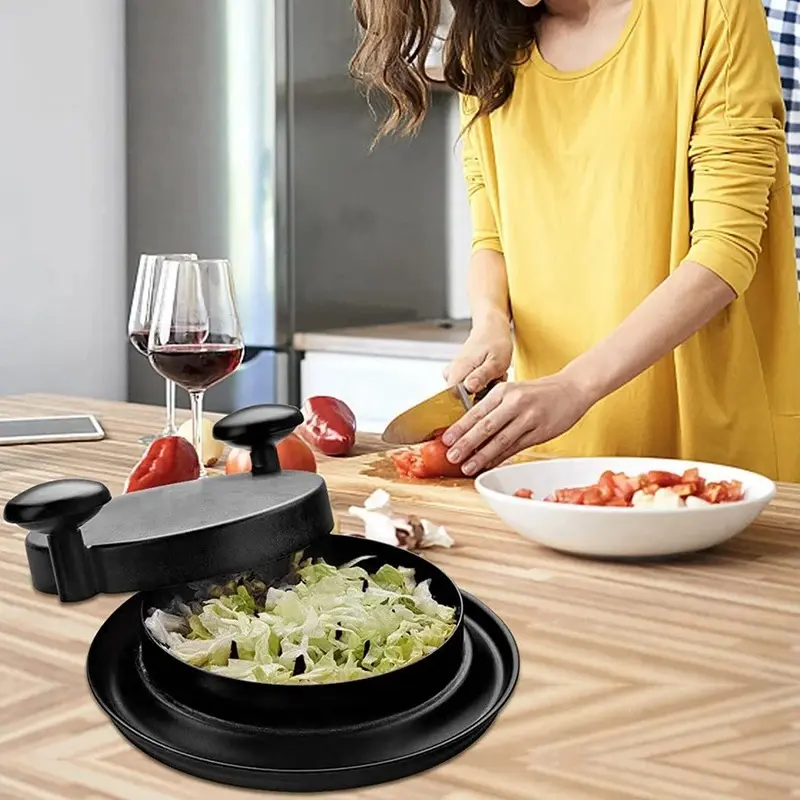 Máquina trituradora de pollo negra sobre mesa de cocina con mujer picando tomates.