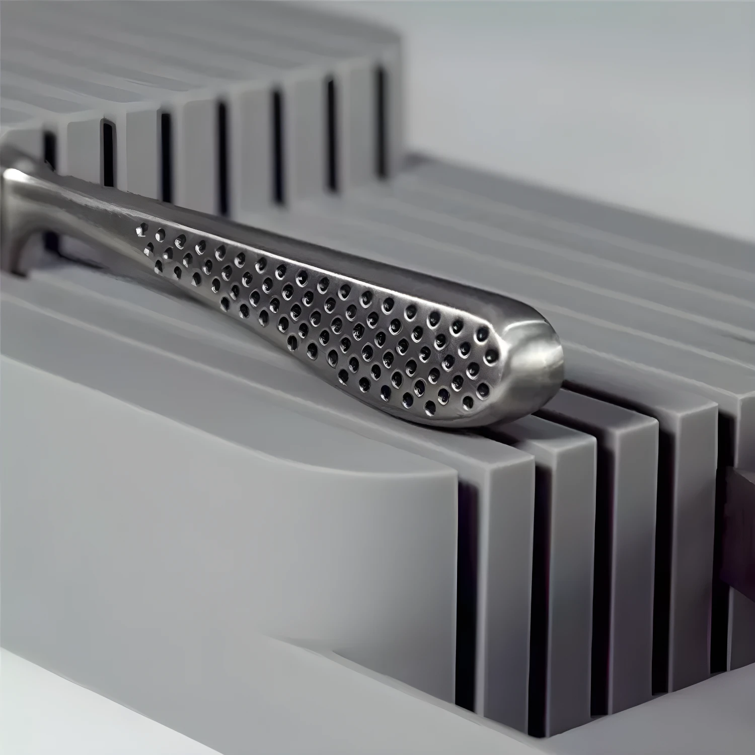 Organizdor de cuchillos plateado con mango perforado, ubicado en un organizador gris con ranuras.