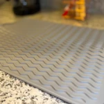 Tapete de silicona para secar platos Gourmet con diseño ondulado gris sobre granito.