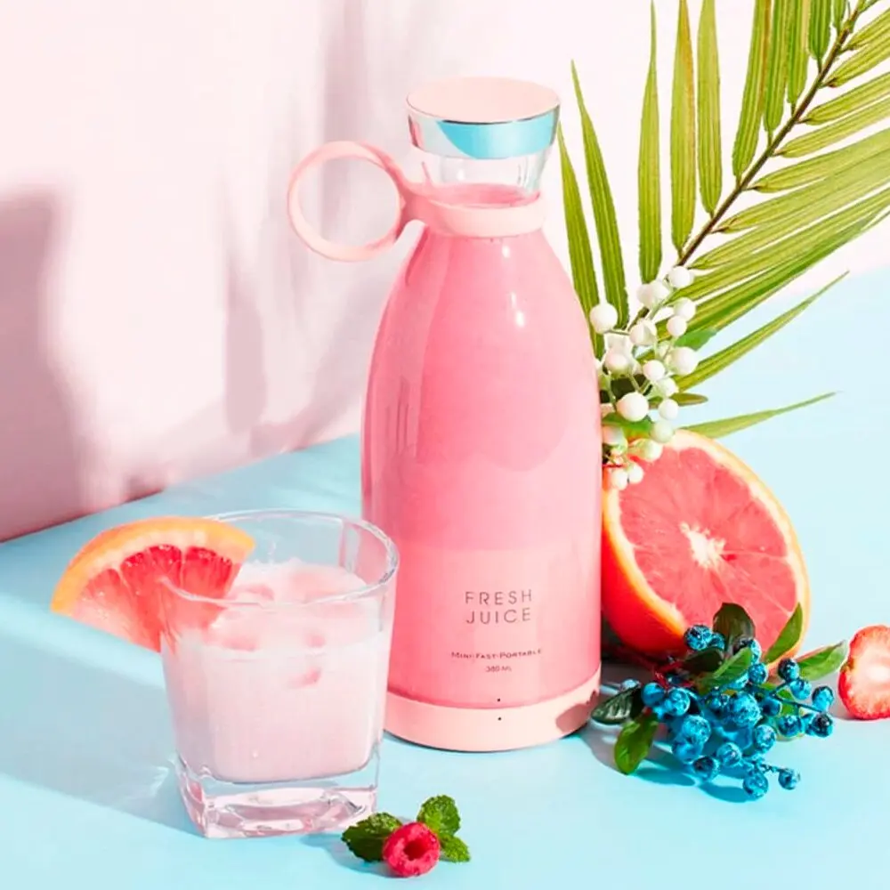Botella mini licuadora portátil rosa con jugo fresco, pomelo y arándanos sobre fondo azul.
