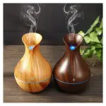 Humidificador difusor de aroma en forma de jarrón de madera clara y oscura con vapor.