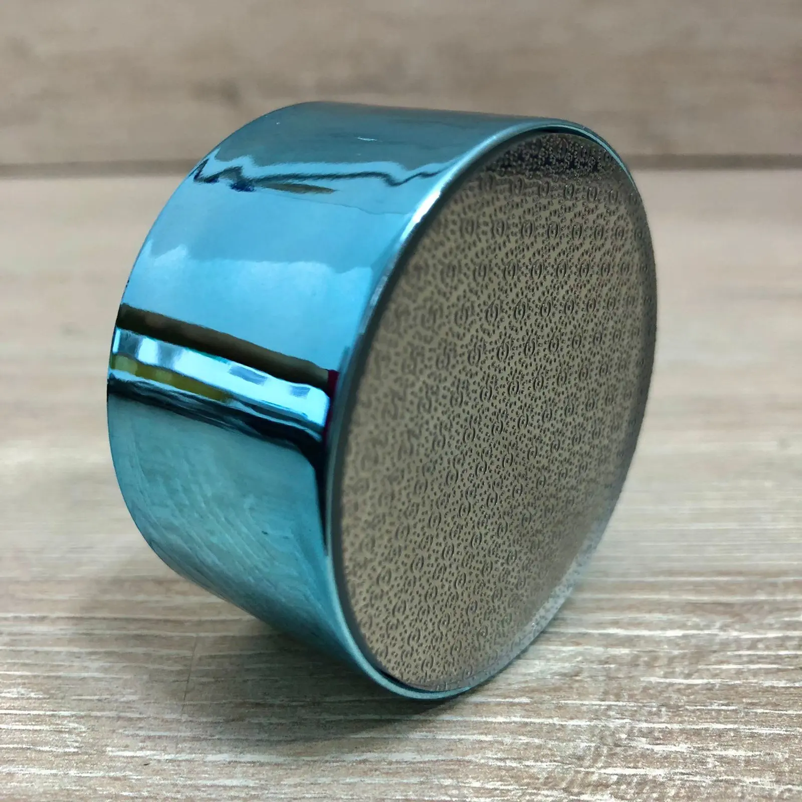 Depilador de cristal azul con superficie texturizada en ángulo lateral sobre madera.