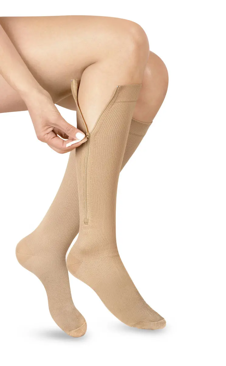 Medias de compresión con cremallera hasta la rodilla, color piel, ajustadas por una mano.