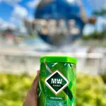 Fibra MW natural en lata verde con tapa brillante, sostenida en mano al aire libre.