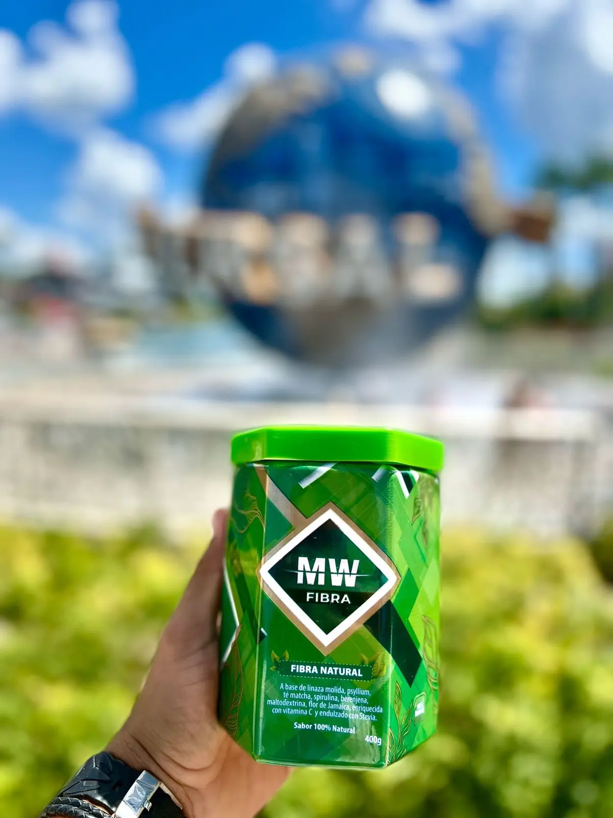 Fibra MW natural en lata verde con tapa brillante, sostenida en mano al aire libre.