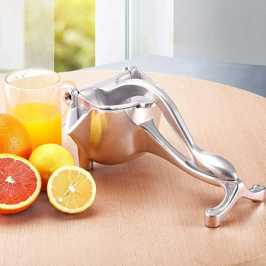 Exprimidor manual de aluminio plateado con jugo de naranja y frutas cítricas sobre mesa de madera.