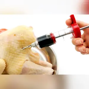 Inyector de carne con jeringa para marinar pollo, con líquido oscuro.